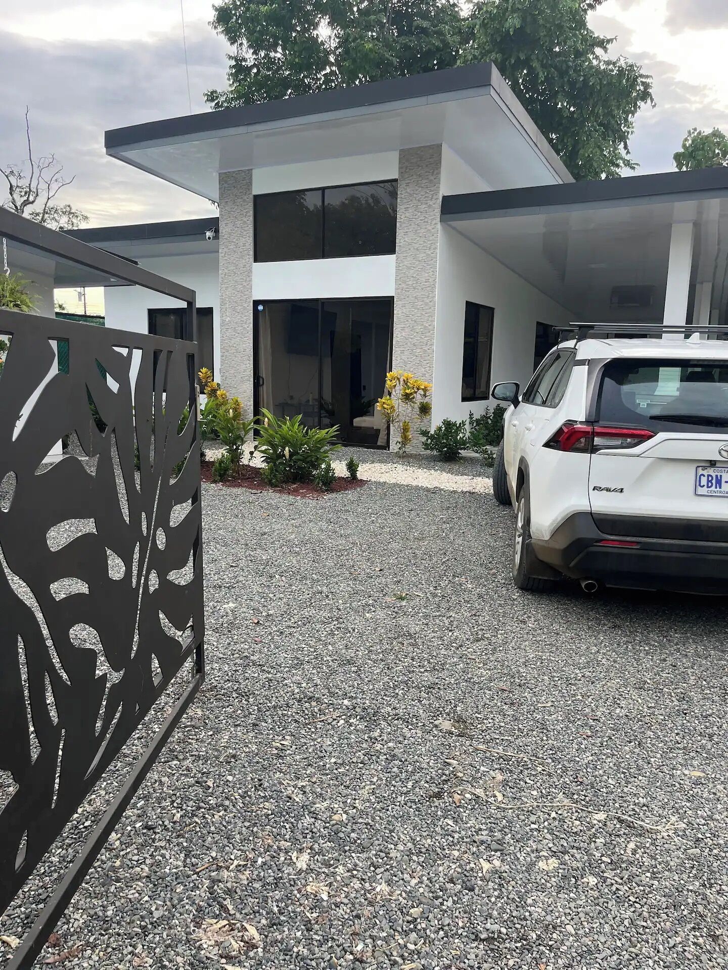 A modern two-story house with a gravel driveway, a white car parked in the driveway, and a decorative metal fence.