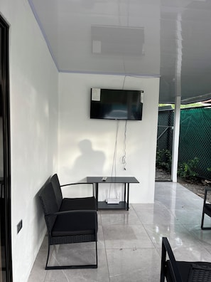 Ein modernes Zimmer mit Wandfernseher, einem Tisch, einem Stuhl und Fliesenboden.