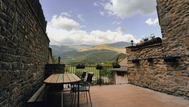 Un patio con paredes de piedra, una mesa y sillas, con vistas a un paisaje montañoso.
