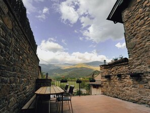 A stone-walled patio with a table and chairs, overlooking a mountainous landscape.