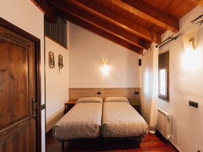Une chambre avec deux lits simples, des poutres apparentes en bois au plafond, un radiateur et une porte.