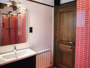 Une salle de bain avec un lavabo blanc, un miroir, une douche et une porte en bois.