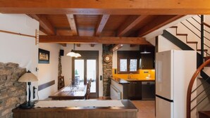 Un interior rústico con vigas de madera a la vista, una pared de piedra, un comedor y una cocina con encimera amarilla.