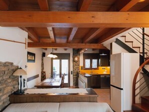 A rustic interior with exposed wooden beams, a stone wall, a dining area, and a kitchen with a yellow countertop.