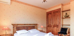 Un dormitorio con cama, armario de madera, una silla y una mesita de noche con lámparas.