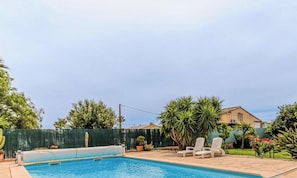 Piscina con sillas de descanso, rodeada de follaje y una cerca.