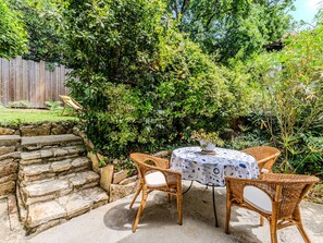 Eine Terrasse mit Korbstühlen und einem Tisch, umgeben von üppigem Grün und einem Holzzaun.