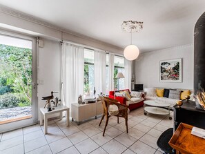 Ein geräumiges Wohnzimmer mit großem Fenster, einem roten Sofa, einem weißen Sessel, einem Esstisch und einem schwarzen Klavier.