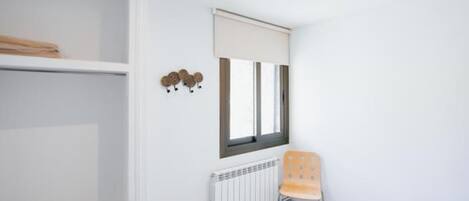 A bedroom with a bed, a radiator, a chair, and a window with blinds.