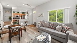 Un salon moderne avec un canapé gris, une table basse en verre et un coin repas comprenant une table et des chaises en bois.
