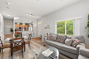 A modern living room with a grey sofa, a glass coffee table, and a dining area with a wooden table and chairs. - Disney Dream~Resort Pool & Water Park Fun~Hot Tub (Kissimmee)