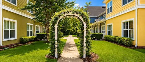 A residential building with a central archway covered in greenery, surrounded by well-maintained lawns and a clear pathway.