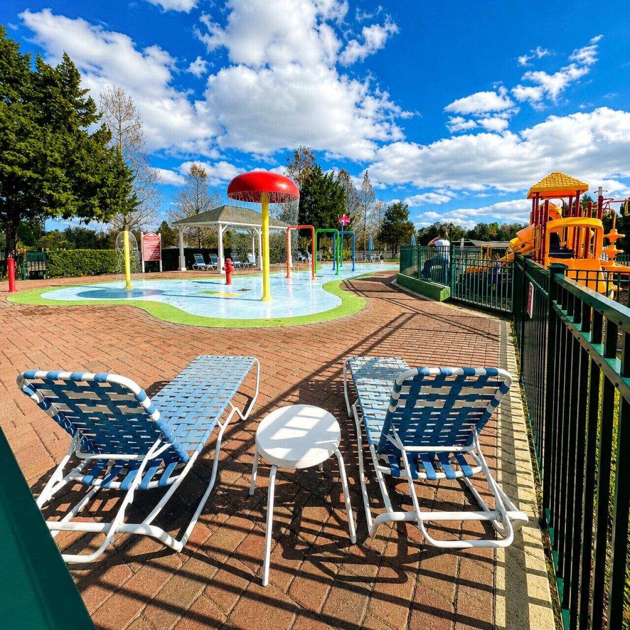 A playground with slides and climbing structures, a water play area, and two lounge chairs with a small table.