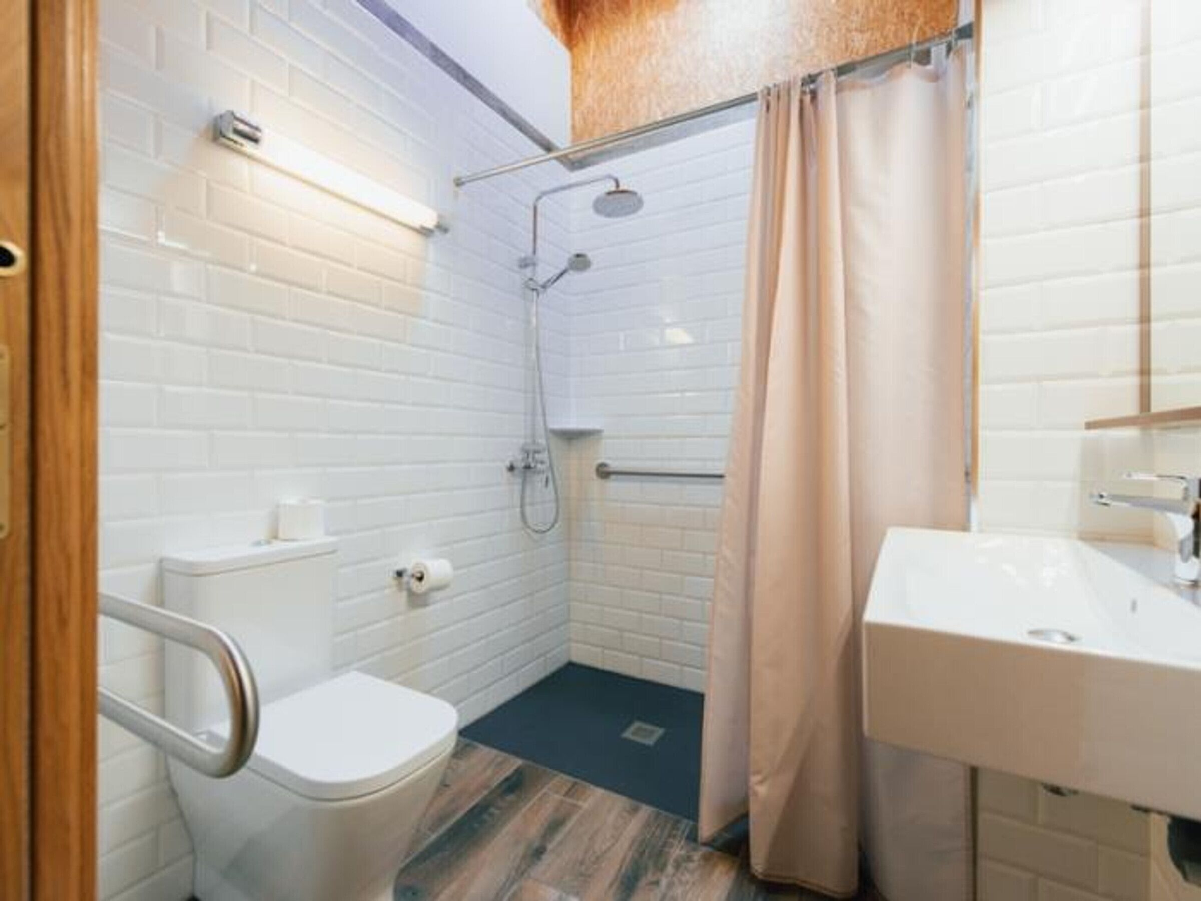 Une salle de bain avec des murs carrelés de carreaux blancs, une douche, des toilettes et un lavabo.