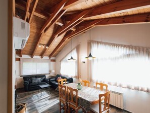 A dining area with a wooden table and chairs, a black sofa, and a window with curtains.