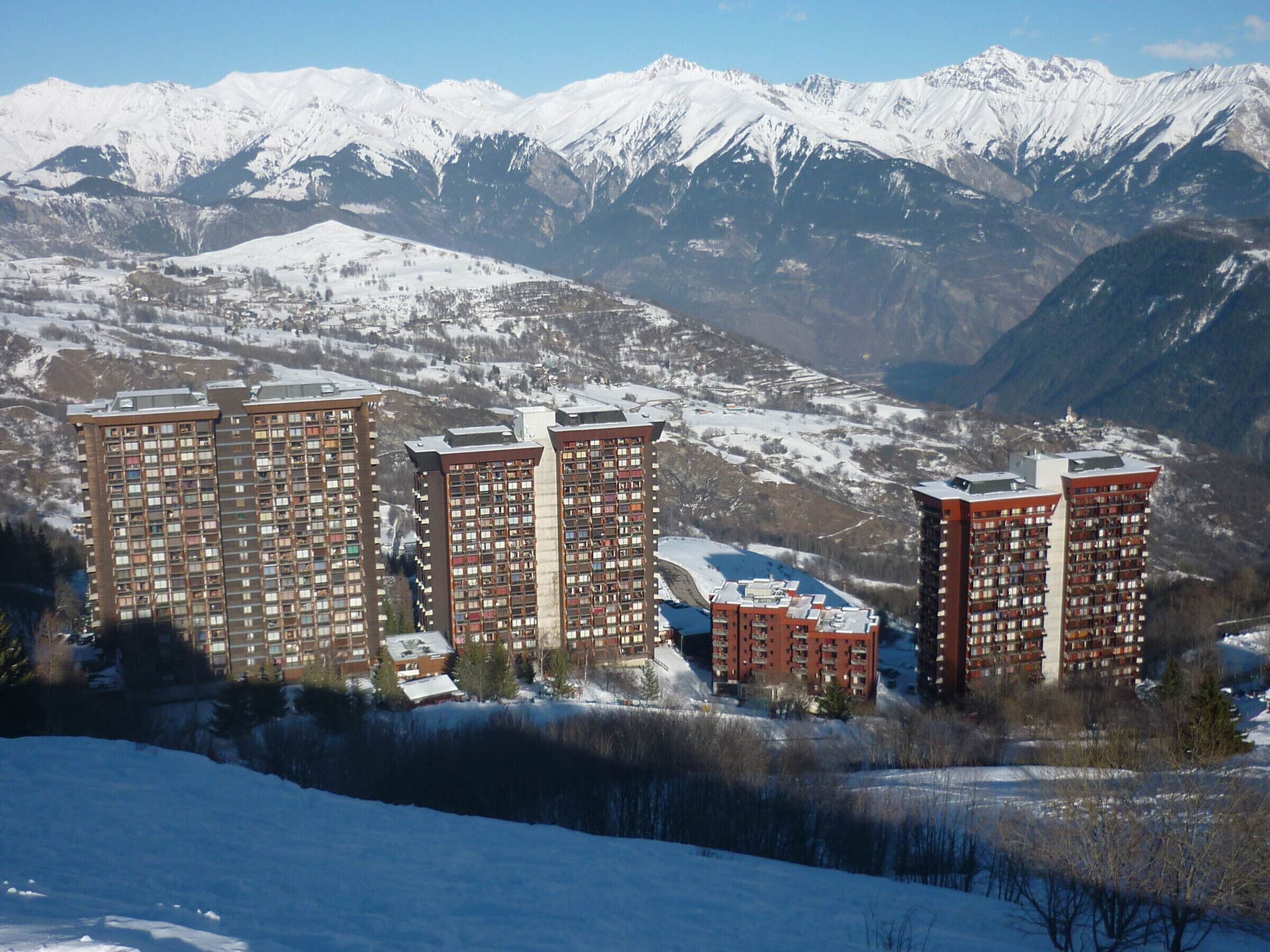 Un ensemble d’immeubles résidentiels de grande hauteur, comprenant de nombreux étages, entouré de montagnes enneigées et surplombant un ciel dégagé.