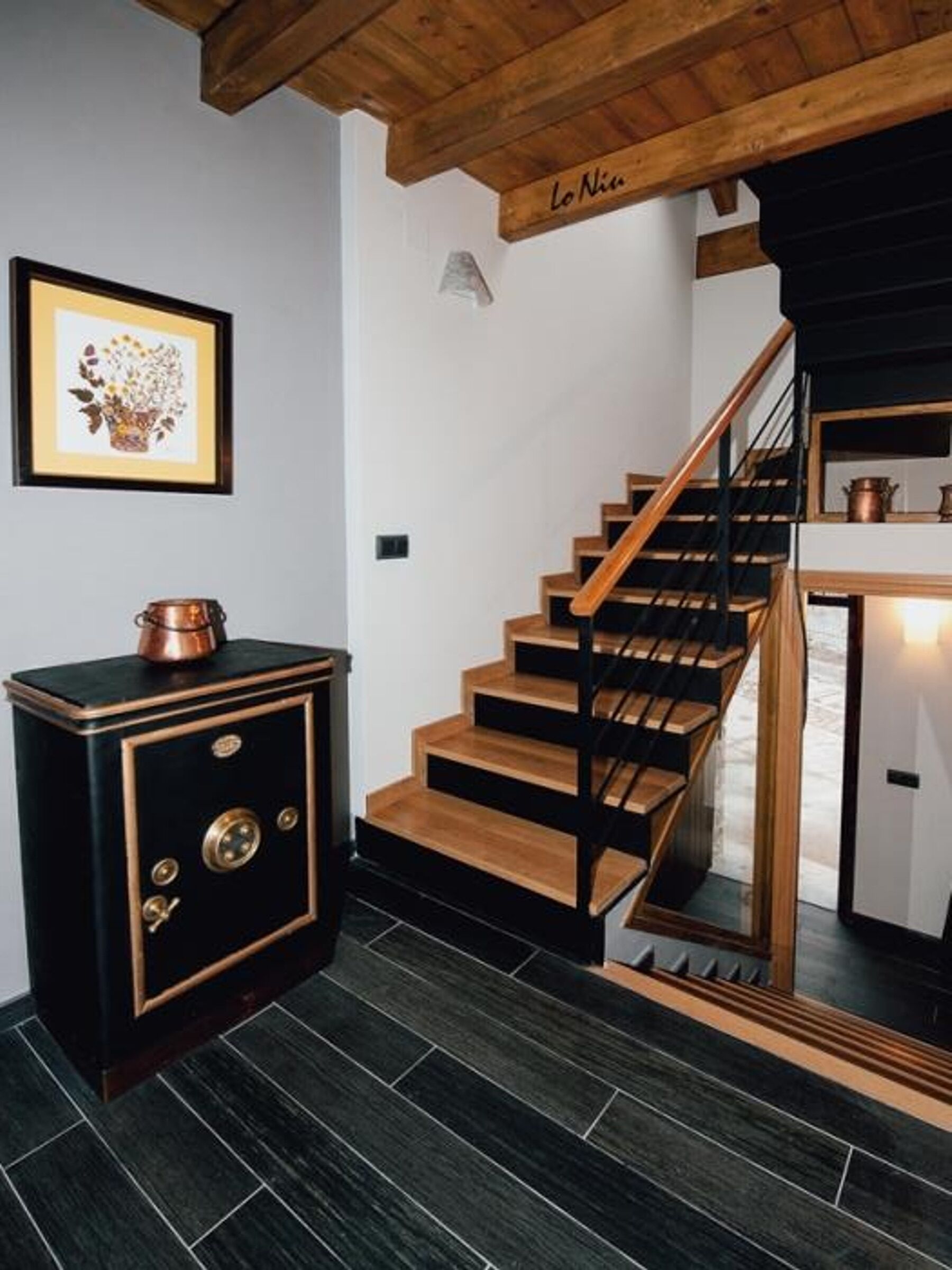 A staircase with wooden steps and black railings, leading to a black and gold cabinet with a copper pot on top.