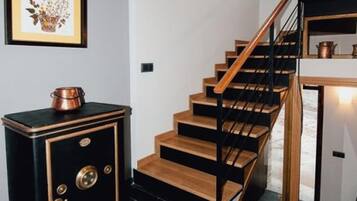 A staircase with wooden steps and black railings, leading to a black and gold cabinet with a copper pot on top.