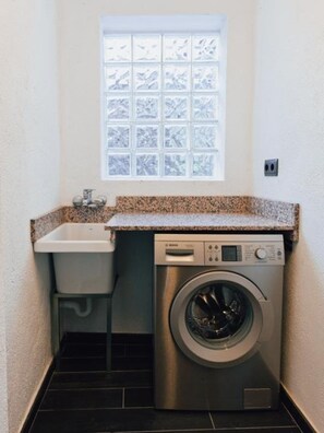 Een kleine wasruimte met een wasmachine, een wasbak en een raam.