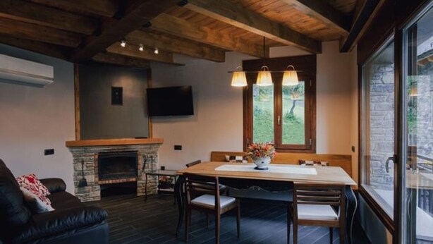 A cozy living room with a fireplace, a dining table with chairs, a sofa, and a TV mounted on the wall. - Cozy House near Aigüestortes Park, 6 ppl, Pets welcome (Espot)