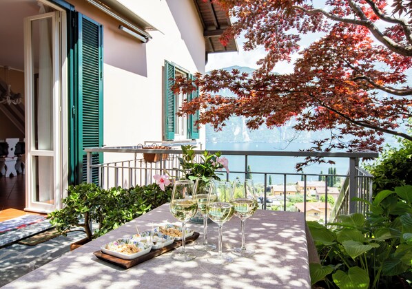 A table with wine glasses and a tray of snacks on a balcony with a view of the sea.