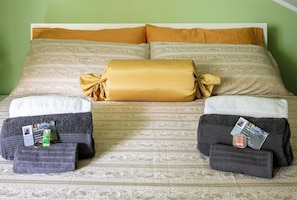 A bed with patterned bedding, two folded towels, and a card on the left side.