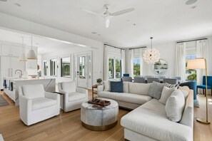 Ein geräumiges Wohnzimmer mit einer großen Eckcouch, einem runden Couchtisch und einem Essbereich mit weißem Tisch und Stühlen.