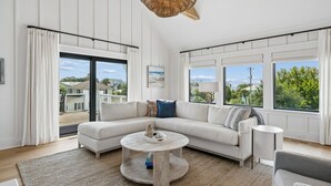 A modern living room with a sectional sofa, a round coffee table, and large windows offering a view of the outdoors. - The Ivory Tide by Charleston Vacays (Isle of Palms)