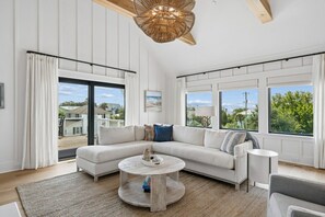 Ein modernes Wohnzimmer mit einer Eckcouch, einem runden Couchtisch und großen Fenstern, die einen Ausblick ins Freie bieten.