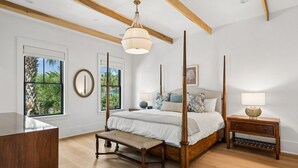 A bedroom with a four-poster bed, wooden beams, a large window, and a bedside table with a lamp. - The Ivory Tide by Charleston Vacays (Isle of Palms)