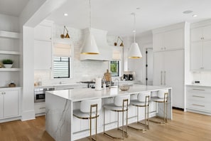 A modern kitchen with white cabinetry, a marble island, and bar stools. - The Ivory Tide by Charleston Vacays (Isle of Palms)