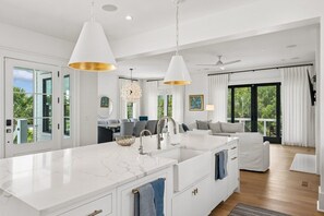 A modern kitchen with a large island, pendant lighting, and a view of the outdoors. - The Ivory Tide by Charleston Vacays (Isle of Palms)