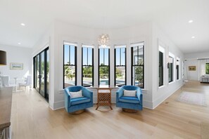 Ein geräumiges Zimmer mit großen Fenstern, Blick auf den Pool und einer Essecke mit zwei blauen Stühlen.