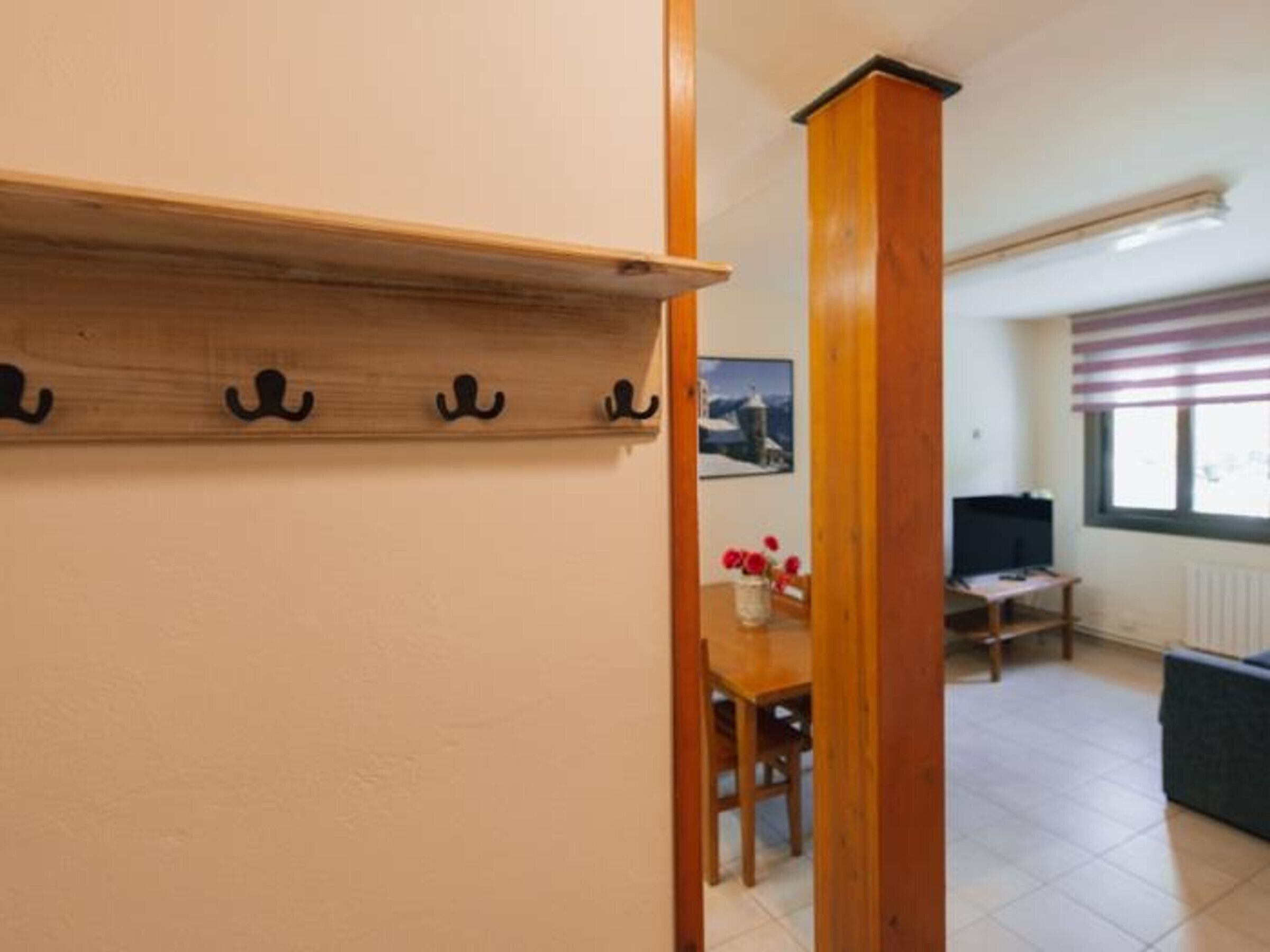 Una habitación con estante de madera y ganchos, una mesa de comedor con sillas, un televisor y una ventana con persianas.