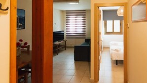 Un pasillo que conduce a un dormitorio con una cama, una mesita y una ventana con persianas.