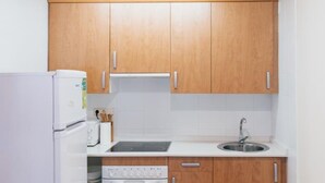Una cocina compacta con armarios de madera, encimera blanca, pileta y horno integrado, además de un refrigerador.