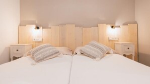 Una cama doble con edredón blanco, dos mesitas de noche y dos lámparas de pared.