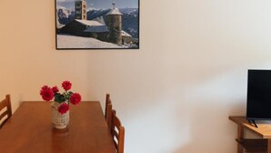 Una mesa de comedor con sillas, un jarrón con flores rojas, un cuadro en la pared y un televisor sobre un mueble.