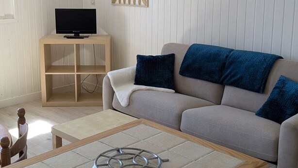 Ein Wohnzimmer mit Sofa, Couchtisch, Fernseher auf einem Schrank und einer Wand mit Spiegel und einem Bilderrahmen.