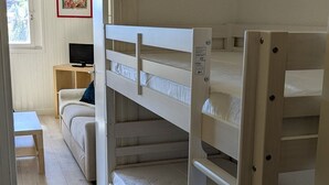 Ein Schlafraum mit Etagenbetten, einem Fernseher auf einem Nachttisch aus Holz, einem kleinen Tisch und einem Fenster.