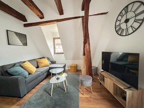 Un salon de style industriel, avec un canapé, une table basse, un téléviseur et des poutres en bois.