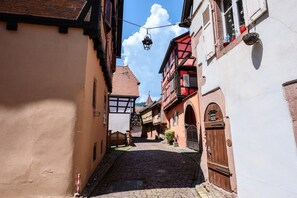 A narrow cobblestone street flanked by traditional buildings with exposed wooden beams and a clear blue sky. - Apartment Le Gîte du Kaiser: Your Comfortable Retreat (Kaysersberg-Vignoble)