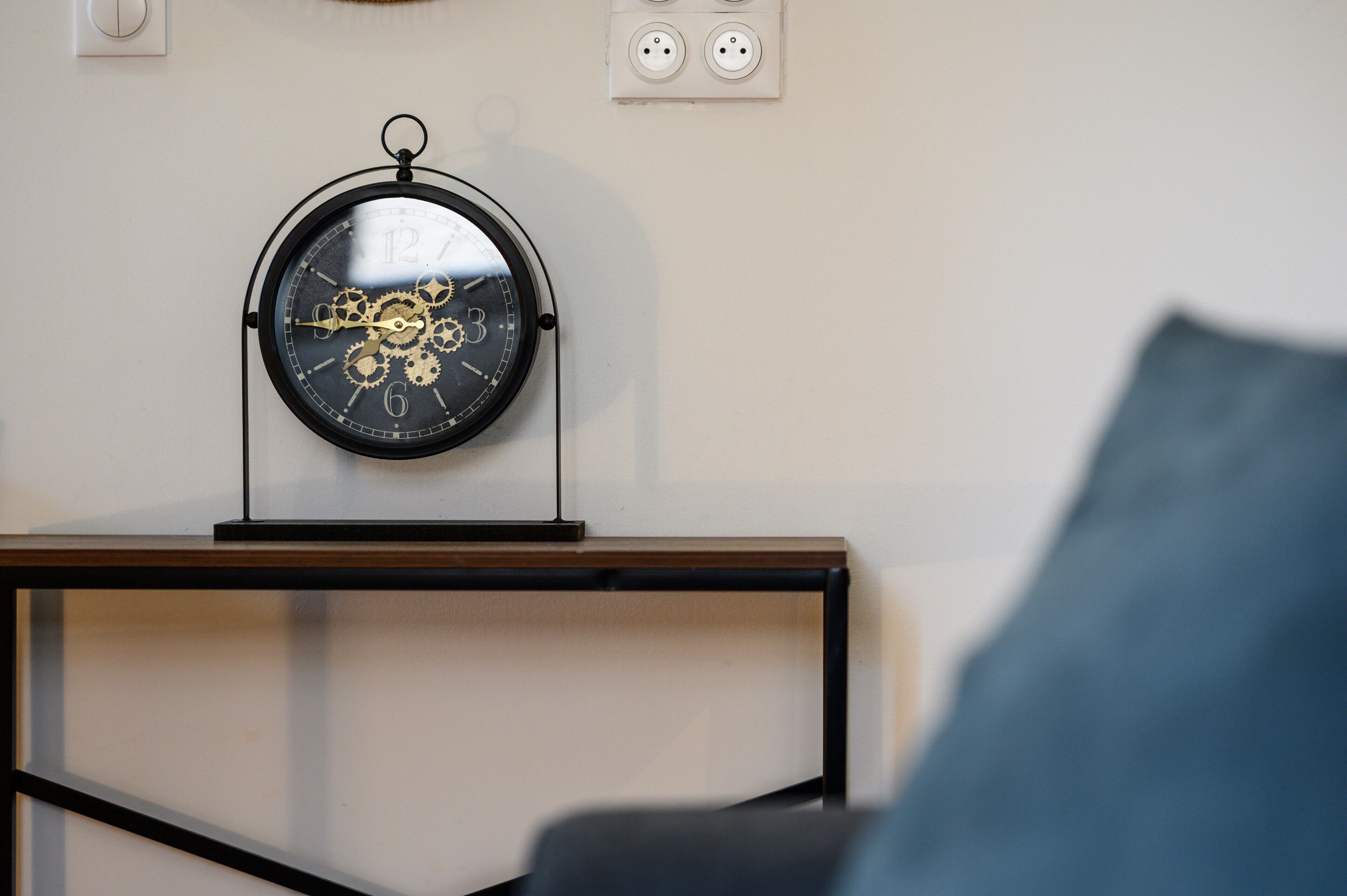 Un reloj de pared con diseño de engranajes, un enchufe y una mesa de madera con estructura metálica negra.