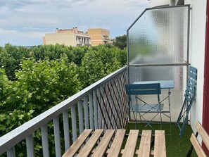 Un balcon avec une table et des chaises en bois, une chaise en métal et un moustiquaire.