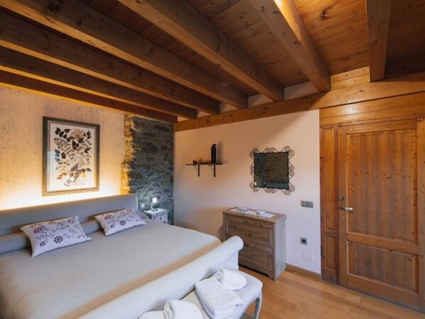Un dormitorio con cama, mesita de noche, cómoda, luz empotrada en la pared y puerta de madera.