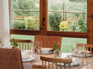 Mesa de comedor lista con sillas, platos y vasos, con vista a un jardín a través de ventanas amplias.