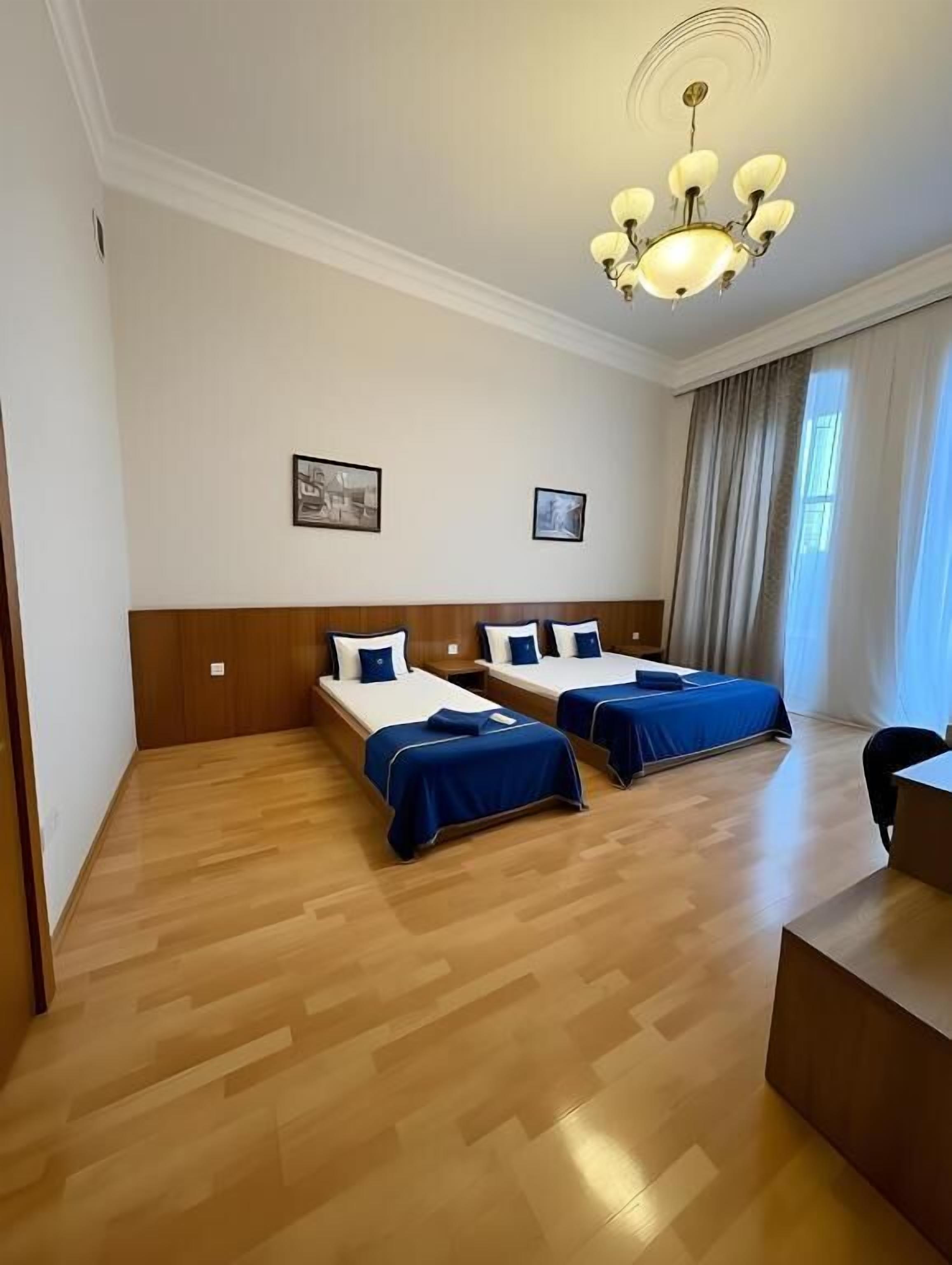 A hotel room with two beds, a wooden floor, a chandelier, and a desk.