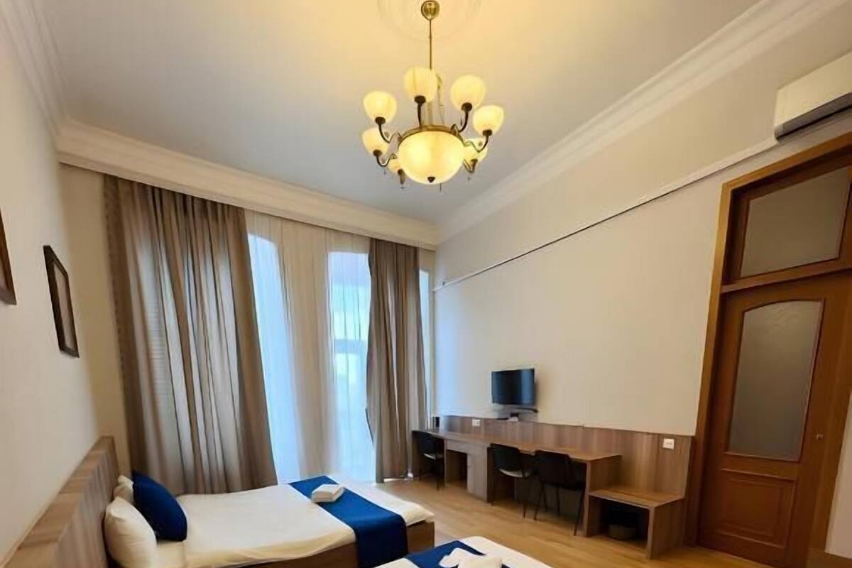 Habitació d'hotel amb dos llits, un escriptori, un televisor i una làmpada de cristall.
