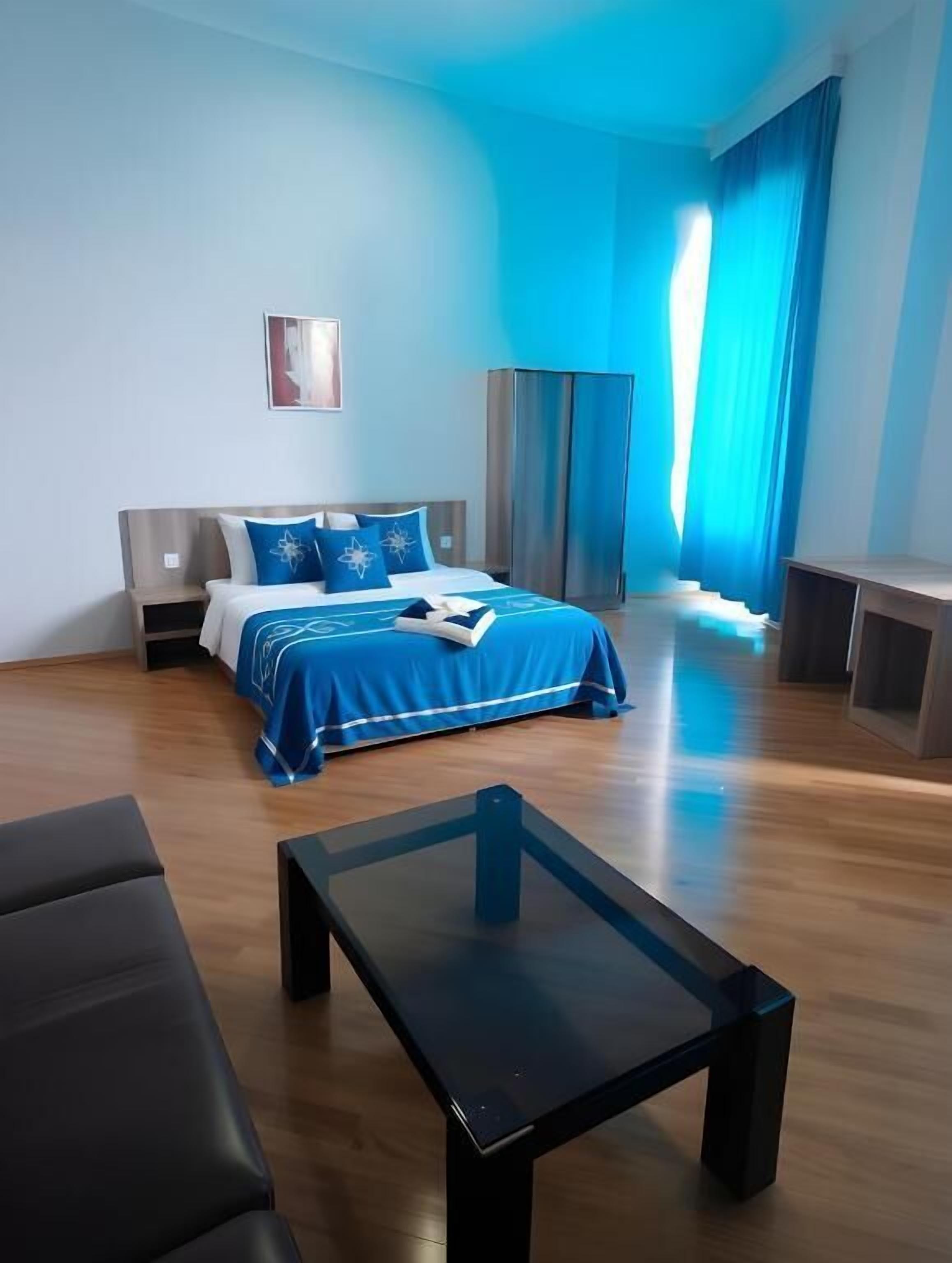 Una habitación de hotel con una cama, una mesita y un ventanal con cortinas.