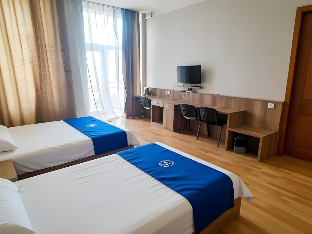 A hotel room with two beds, a desk with a TV, and a window with curtains.